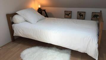 Ein Einzelbett mit weißer Bettwäsche, ein kleiner runder Tisch mit Lampe und drei Wanddekorationen mit Tiermotiven.