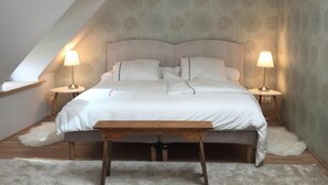 Une chambre avec un plafond en pente, un lit avec une literie blanche, deux lampes de chevet et un banc en bois placé devant le lit.