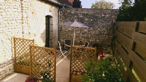 Un espace patio agrémenté de murs en pierre, de jardinières en treillis de bois ornées de fleurs et de mobilier d’extérieur.