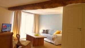 Un salon chaleureux avec un plafond en bois, un canapé blanc, une petite table, un fauteuil en osier et un téléviseur.