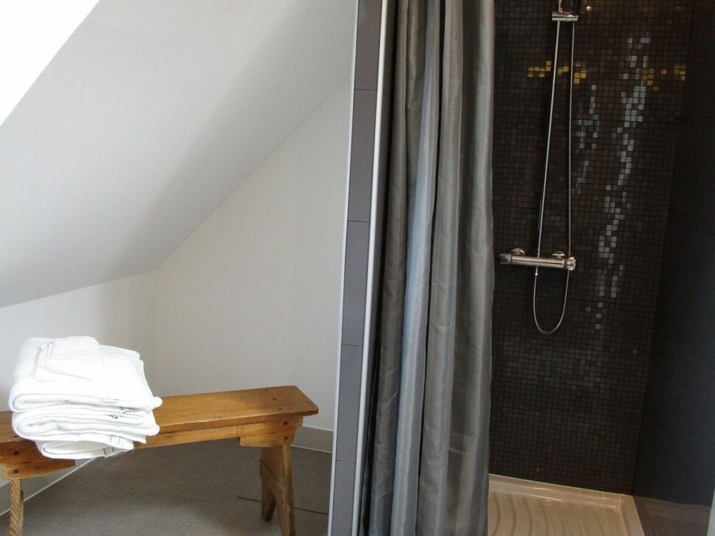 Ein Badezimmer mit Dusche, einer Holzbank und einem Stapel weißer Handtücher.