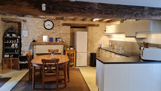 Une cuisine chaleureuse avec une table à manger en bois, des placards blancs et des poutres apparentes.