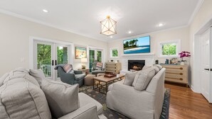 A spacious living room with a fireplace, a television mounted above it, and a large window with a view of the outdoors.