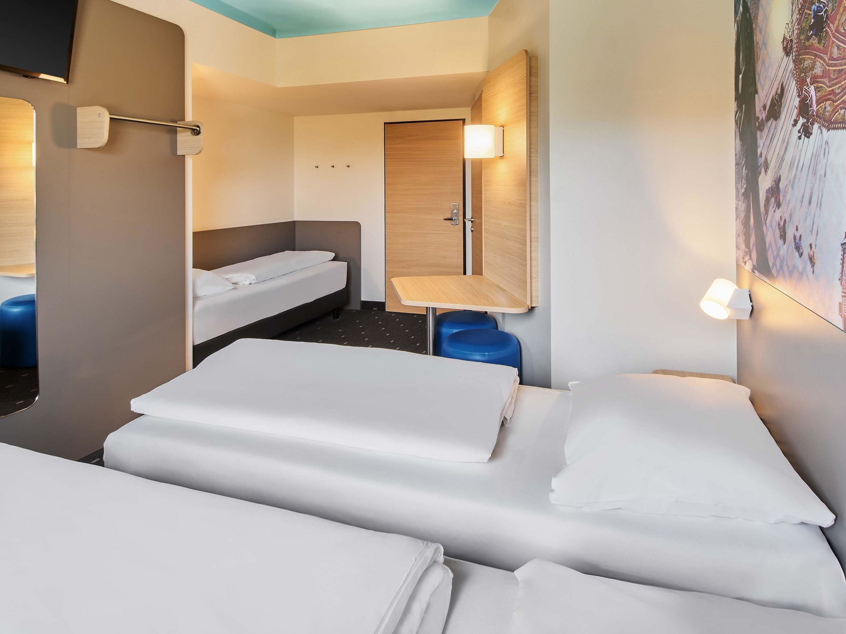 A hotel room with two beds, a small table, a chair, a wardrobe, and a TV.