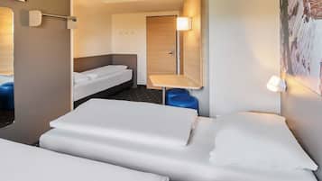 A hotel room with two beds, a small table, a chair, a wardrobe, and a TV.