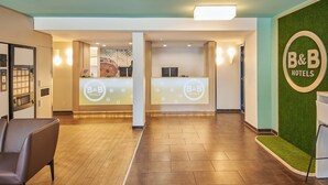 A reception area with a B&B Hotels sign, a reception desk, a waiting area with a chair, and a green wall with artificial grass. - B&B Hotel Darmstadt (Darmstadt)