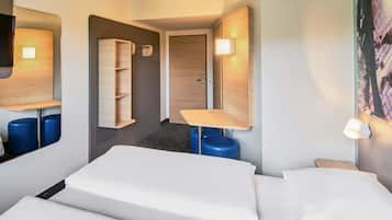 A hotel room with a bed, a desk, a chair, a wardrobe, and a painting on the wall.