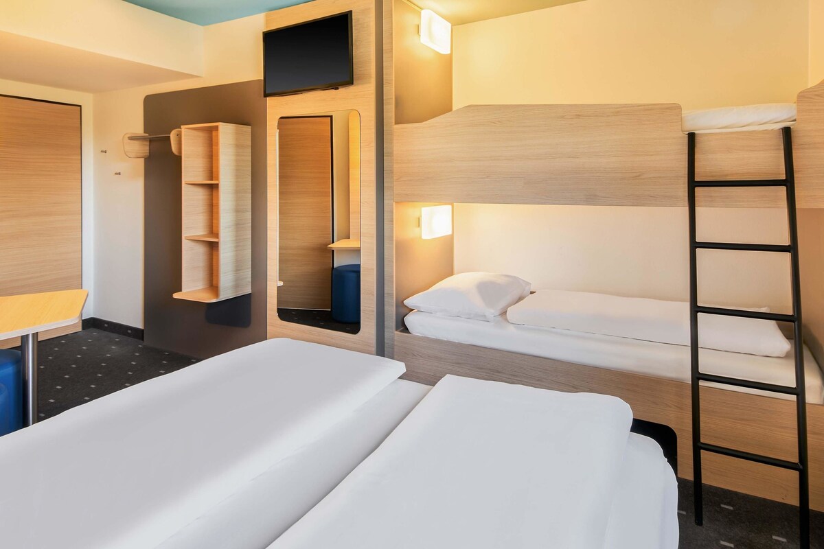 A hotel room with two beds, a wardrobe, a mirror, and a TV.
