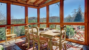 A wooden dining area with large windows, a table set for four, and chairs. - Breathtaking views,private property,glass porch w/wood-burning fireplace (Highlands)