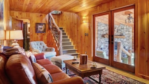 A wooden interior with a staircase, leather sofas, a wooden coffee table, and a stone wall visible through a glass door. - Breathtaking views,private property,glass porch w/wood-burning fireplace (Highlands)