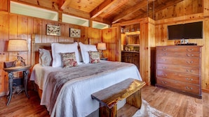 A wooden cabin bedroom with a bed, dresser, and a television. - Breathtaking views,private property,glass porch w/wood-burning fireplace (Highlands)