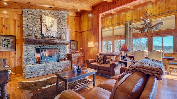 A cozy log cabin interior with a stone fireplace, leather furniture, and large windows. - Breathtaking views,private property,glass porch w/wood-burning fireplace (Highlands)
