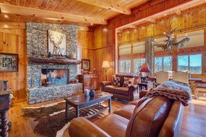 A cozy log cabin interior with a stone fireplace, leather furniture, and large windows. - Breathtaking views,private property,glass porch w/wood-burning fireplace (Highlands)