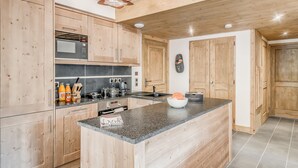 A modern kitchen with wooden cabinets, a granite countertop, and a unique ceiling light fixture. - Luxury 5-room in Tignes, 8-10 people, hotel service (Tignes)