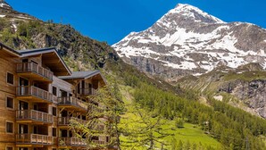 A wooden multi-story building with balconies, set against a backdrop of a snow-capped mountain and a clear blue sky. - Luxury 5-room in Tignes, 8-10 people, hotel service (Tignes)