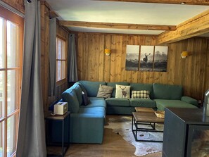 Une pièce chaleureuse avec des murs en bois, un canapé vert, une petite table et une fenêtre avec des rideaux.
