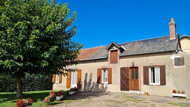 A traditional building with a gravel driveway, wooden shutters, and a brick chimney.