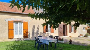 A rustic building with a tiled roof, a wooden door, and a table with chairs in the yard.