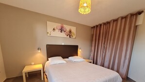 Un lit bien fait, avec une tête de lit, une table de chevet et un luminaire fixé au mur.