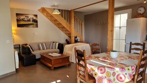 Un salon comprenant un canapé, une table basse et une table à manger avec des chaises. Un escalier mène à une autre pièce.