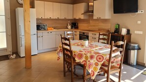 Une cuisine avec des meubles blancs, un four à micro-ondes et un évier. On y trouve une table à manger avec des chaises et une nappe à motifs.