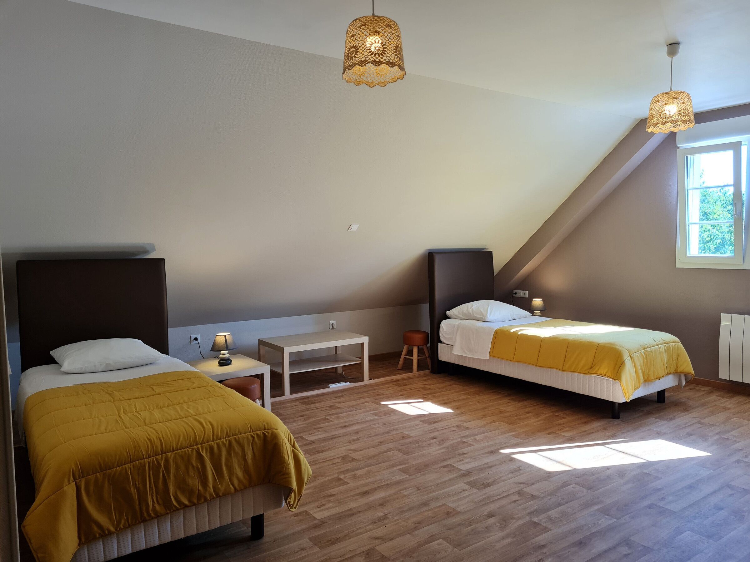 A modern bedroom with two beds, a small table, and a bench.