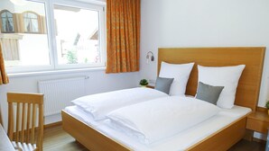 Un lit double avec du linge de lit blanc, une tête de lit en bois et une table de chevet avec une lampe.