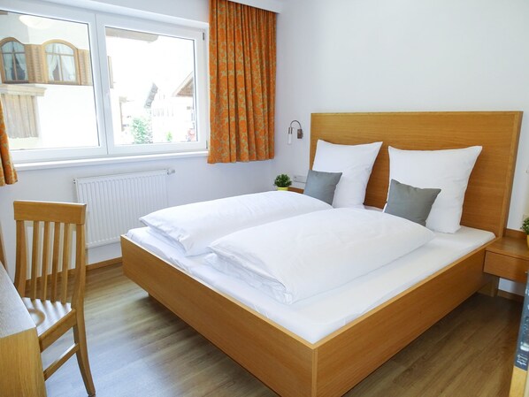 A double bed with white linens, a wooden headboard, and a nightstand with a lamp.