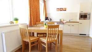Une cuisine moderne avec des meubles blancs, un four encastré et un coin repas comprenant des chaises et une table en bois.