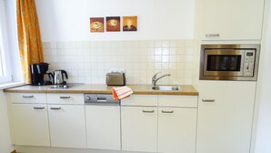 Une cuisine avec des armoires blanches, un plan de travail en bois, un évier en acier inoxydable, un grille-pain, une machine à café et un four à micro-ondes.
