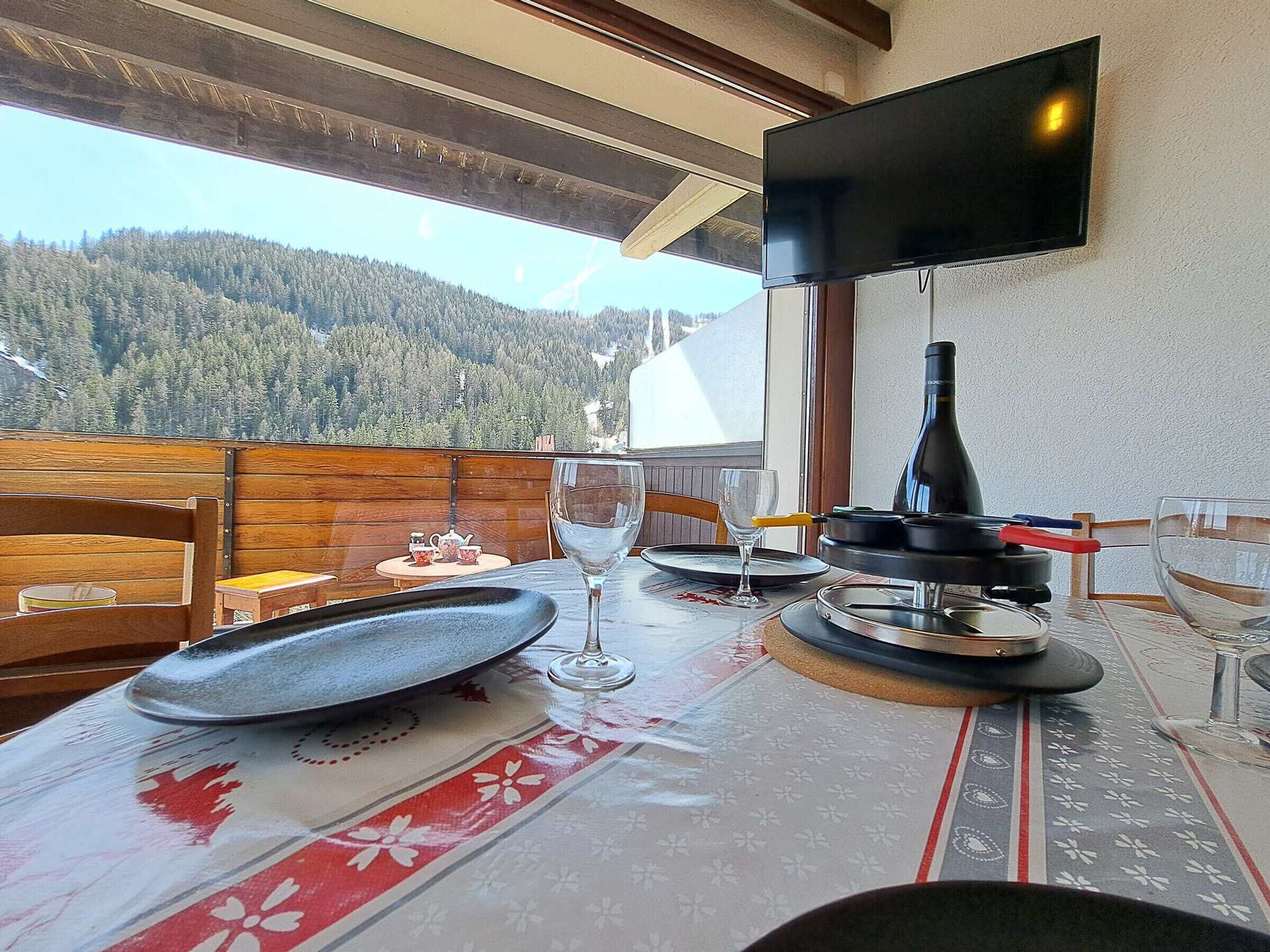 Un comedor con una mesa dispuesta para dos personas, una botella de vino y un televisor montado en la pared.
