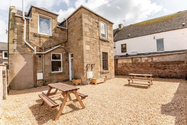 A stone building with a gravel courtyard, wooden benches, and a picnic table. - No 67 Leuchars (Nr St Andrews) Free Parking - Pet Friendly (Leuchars)