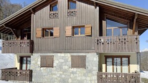 Eine zweistöckige Holzhütte mit Steinwänden, Holzbalkonen und zahlreichen Fenstern mit Fensterläden.