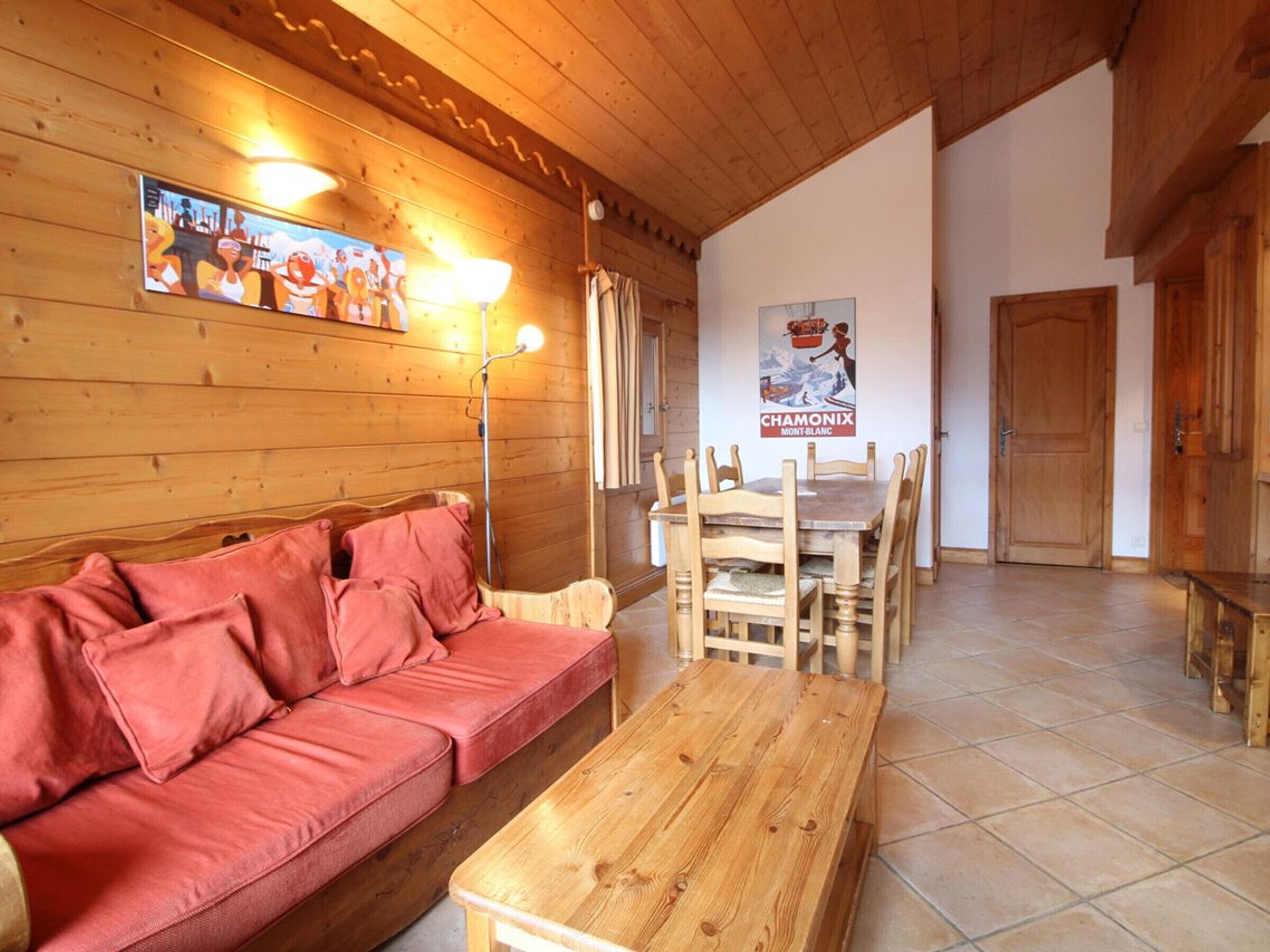 Une pièce chaleureuse avec un plafond en bois, un canapé rouge, une table en bois et une affiche accrochée au mur.