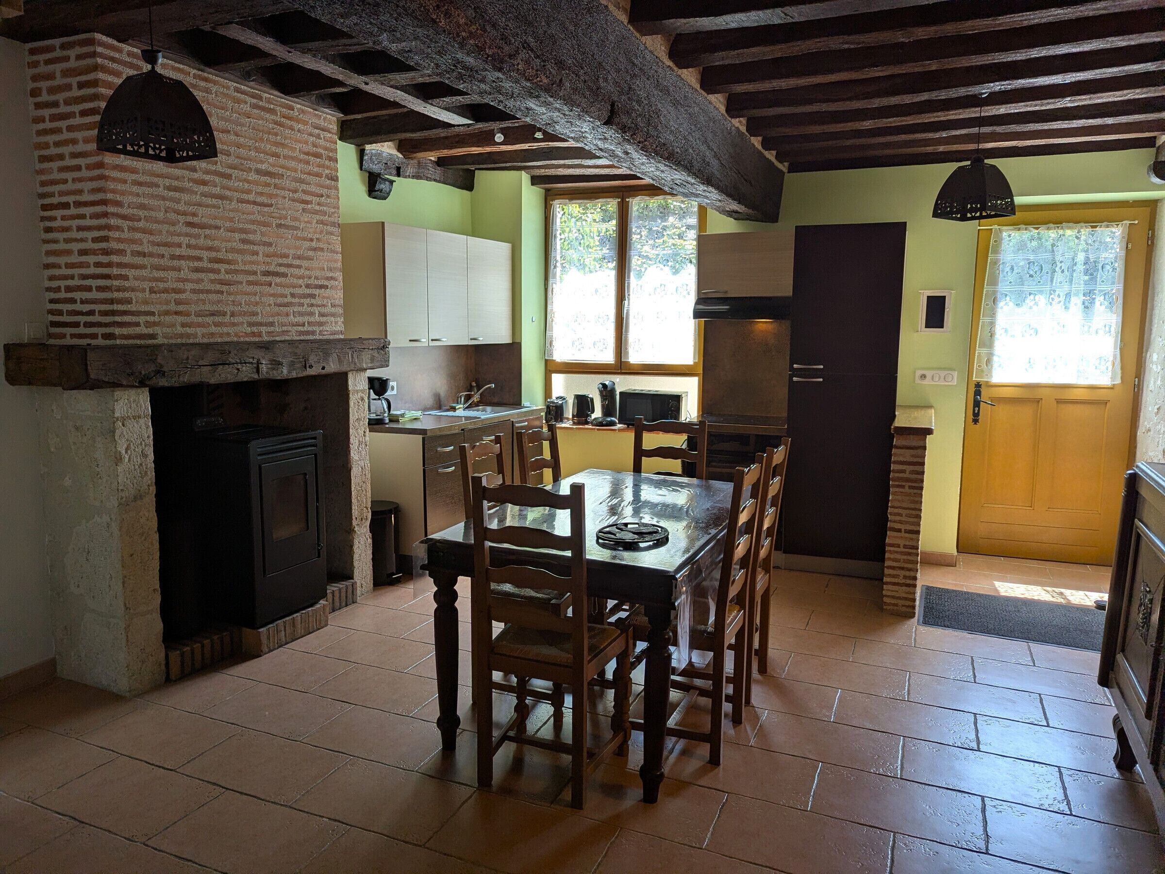 Une cuisine rustique avec une cheminée en briques, une table à manger en bois et un petit îlot central doté d’un évier.