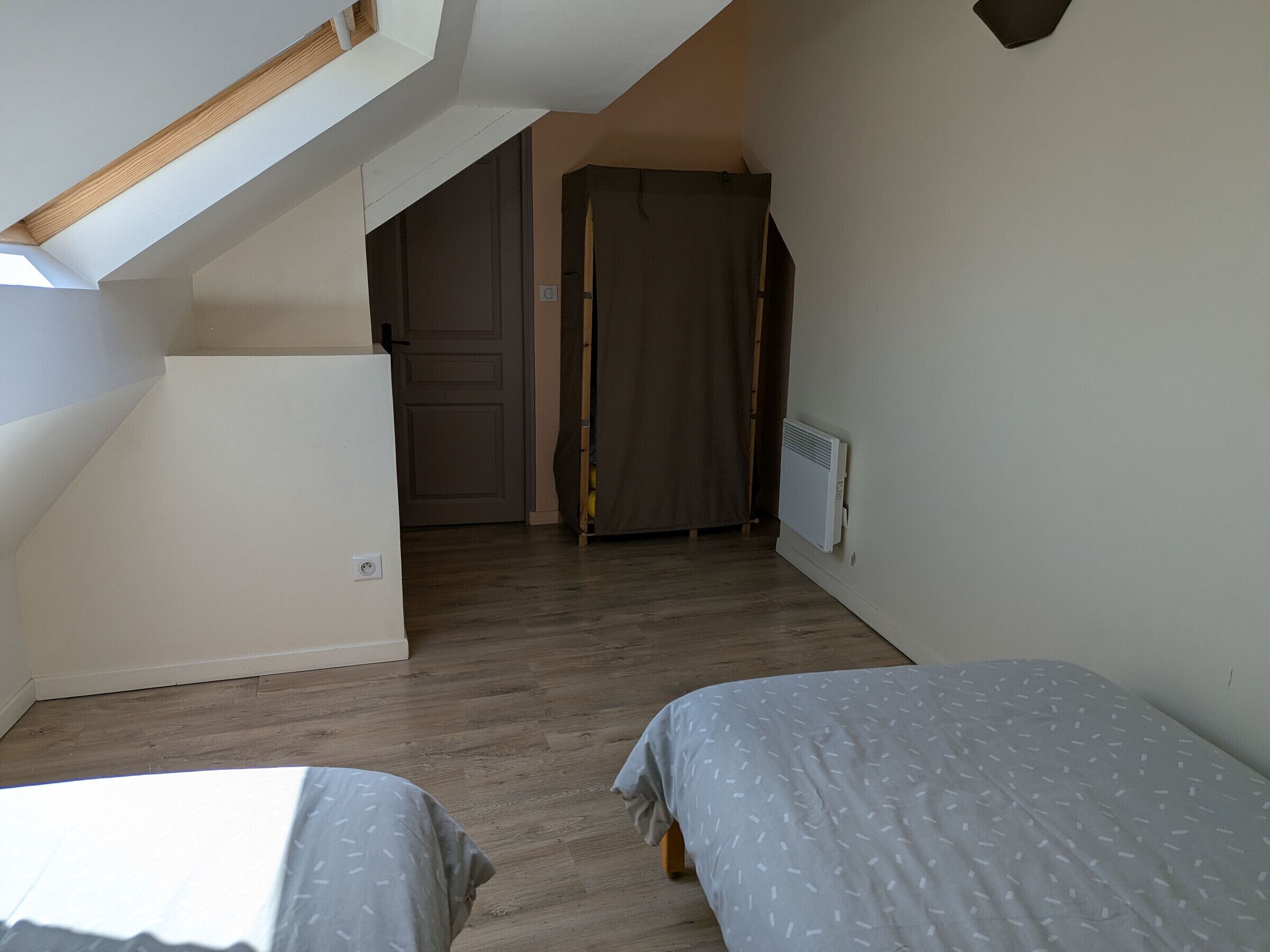 Une chambre avec deux lits, un radiateur, une porte et un escalier.