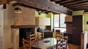 Una cocina rústica con vigas a la vista, un horno de ladrillo, sillas de madera y una mesa de comedor.