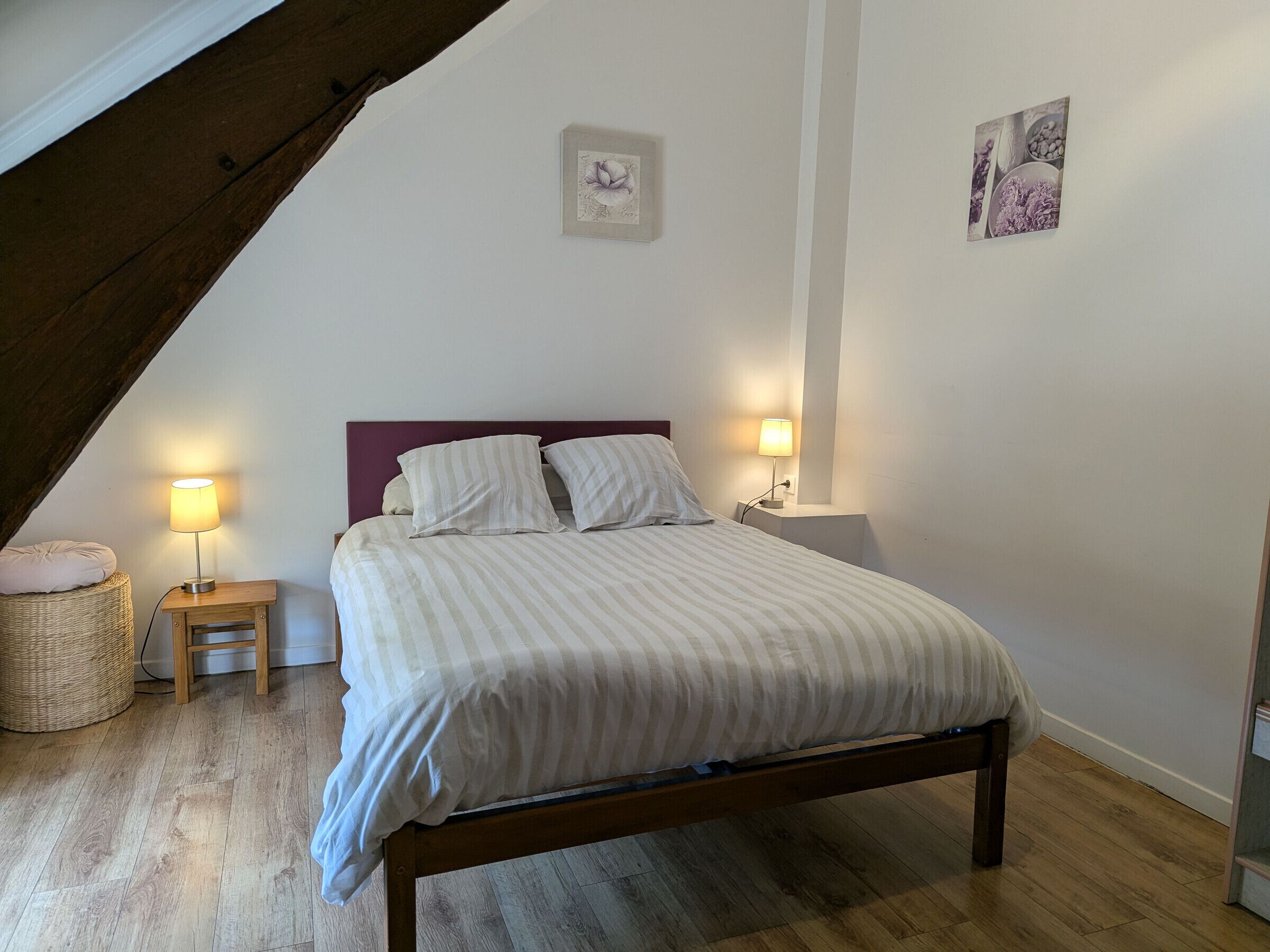 A bedroom with a bed, two bedside tables, a lamp, a wall-mounted picture, and a wooden floor.