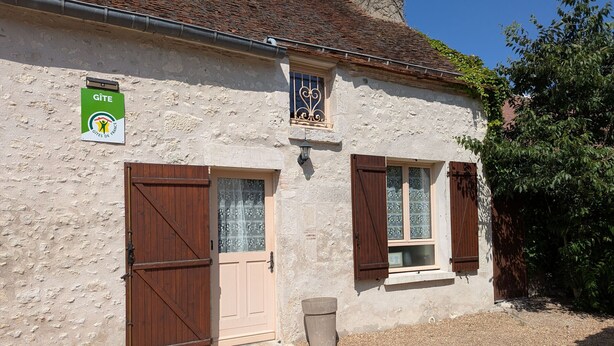Un edificio con un cartel de Gîte de France, una puerta de madera grande, una ventana con contraventanas y un cubo de basura pequeño.