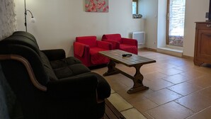 Una sala de estar con un sofá, dos sillas rojas, una mesa de centro, una lámpara, un cuadro, un radiador y una ventana.