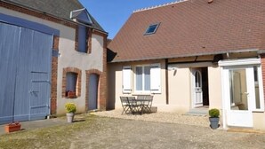 Une maison à deux étages avec un toit recouvert de tuiles, un patio couvert avec une table et des chaises, et une porte de garage bleue.