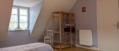 A bedroom with two beds, a wooden wardrobe, a radiator, and a window with curtains.