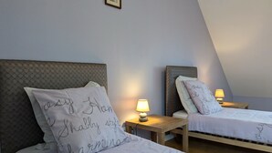 Deux lits jumeaux avec des têtes de lit, chacun étant muni d’une table de chevet et d’une lampe. Les murs sont de couleur unie et un tableau encadré est accroché au-dessus des lits.