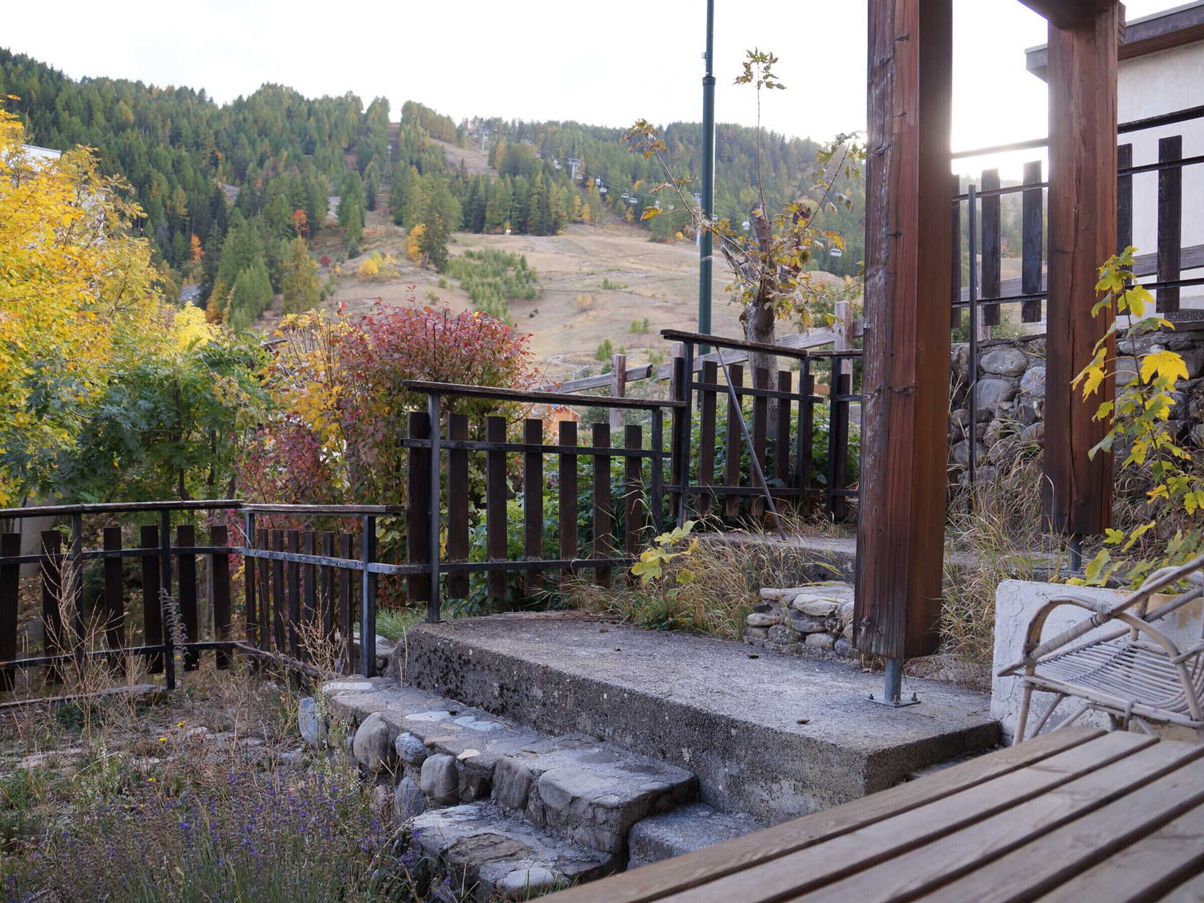 Une terrasse en bois avec des marches menant à un mur de pierre, le tout entouré d’une clôture en bois et agrémenté de diverses plantes.
