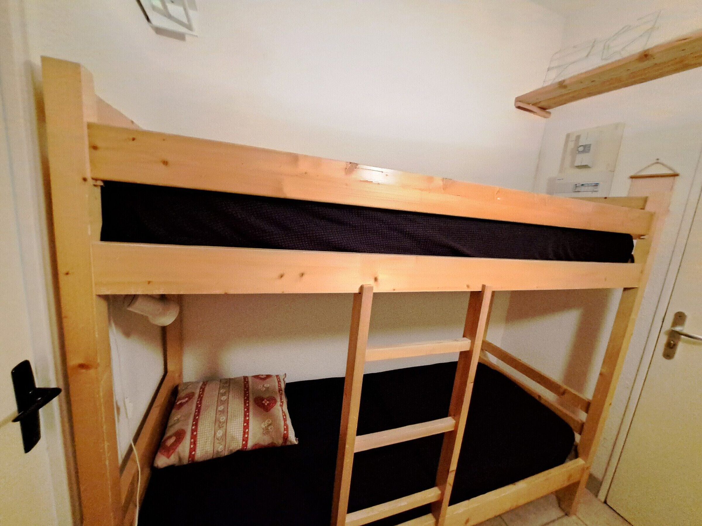 A bunk bed with a ladder, a pillow, and a small shelf.