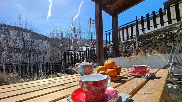 A wooden table with a red floral teapot and cups, oranges, and a bicycle.