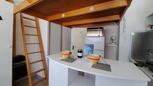 A compact kitchen with a white countertop, a refrigerator, a coffee maker, and a ladder against the wall.
