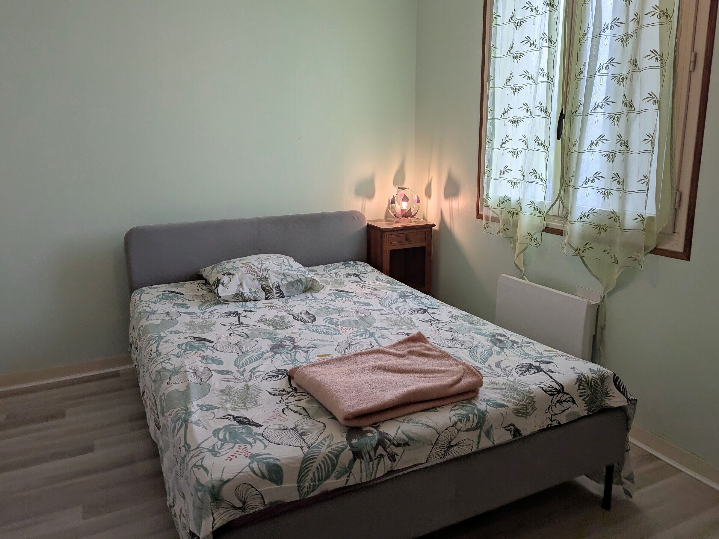 Un letto singolo con una coperta a fiori, un comodino con una lampada e una finestra con tenda in bambù.