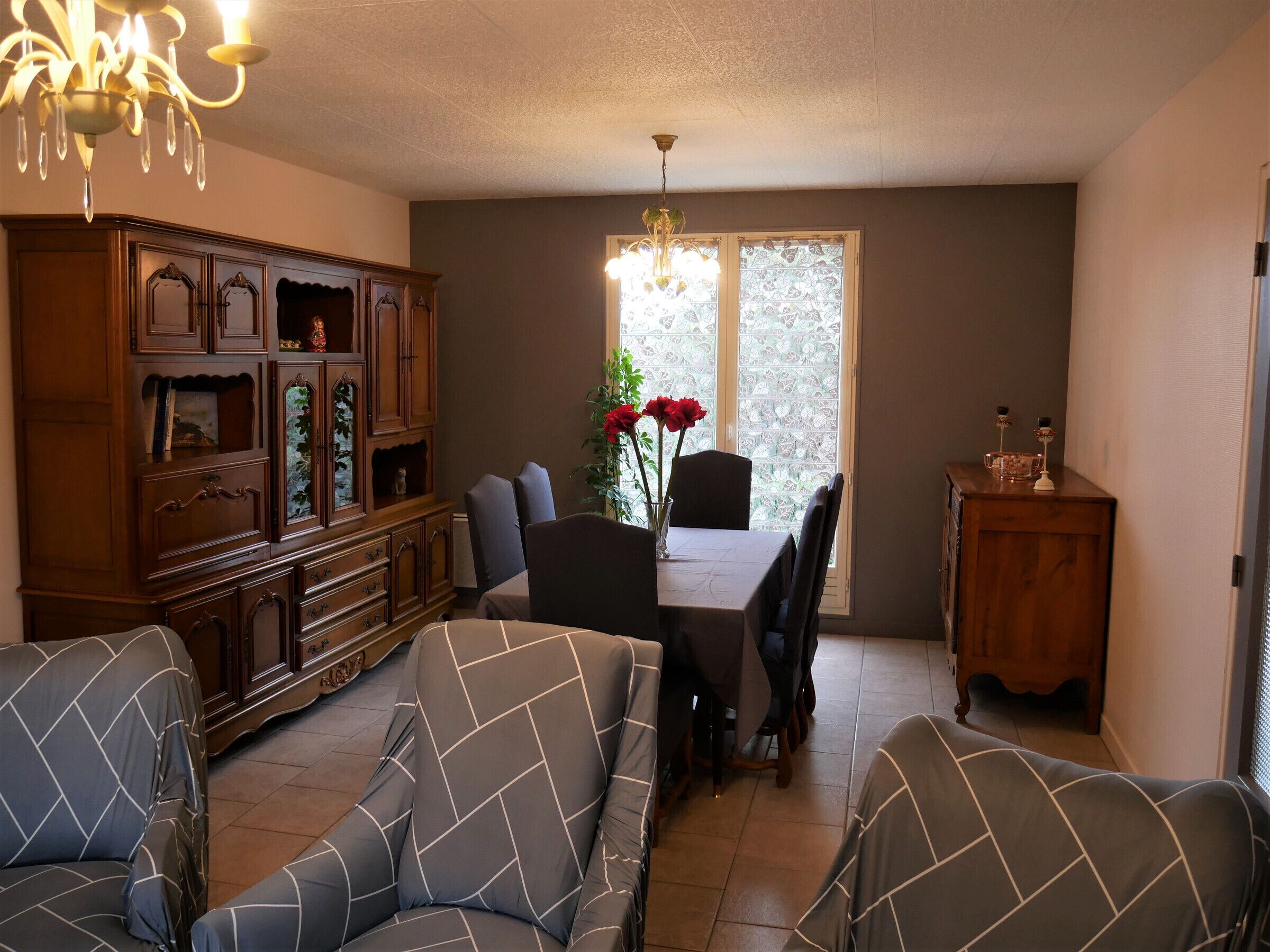A dining area with a table and chairs, a chandelier, and a cabinet with decorative items.