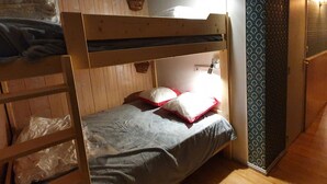 Een slaapkamer met een stapelbed van hout, een enkel bed met kussens, een wandplank en een behang met patroon.